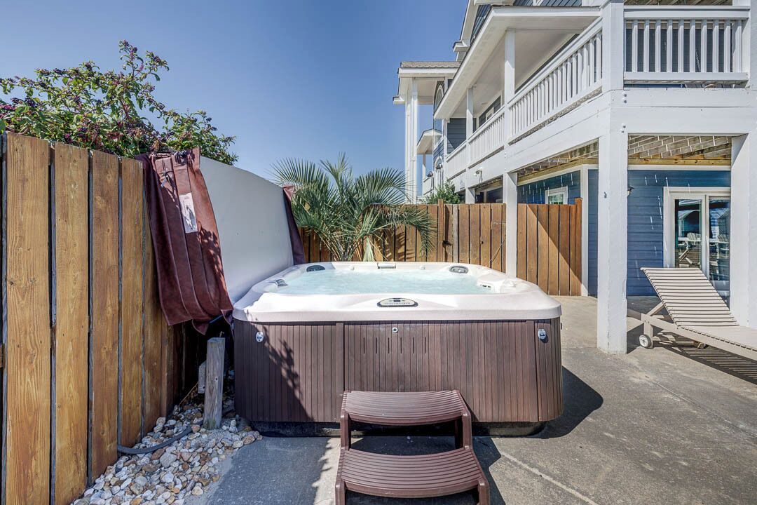 A hot tub in a backyard with a wooden fence, a chair, and a balcony with a chair.