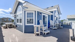 A blue building with white trim, a covered deck with Adirondack chairs, and a small table. - Corolla Coastin | 740 ft to the beach | Private Pool, Hot Tub (Corolla)