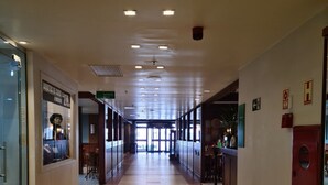 Un couloir d’hôtel avec un sol carrelé, des portes en verre sur la gauche et un comptoir d’accueil sur la droite.