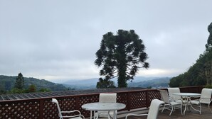 Une terrasse avec des sièges extérieurs, une vue sur des collines lointaines et un grand arbre.