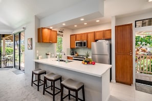 Enjoy cooking in this kitchen with a large island, sink, and stools, offering a view of the outdoor patio area.