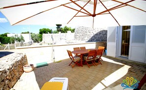 An outdoor patio with a table and chairs, a yellow lounge chair, and a stone wall.