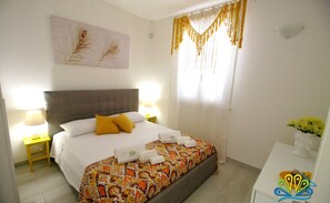 A hotel room with a large bed, a headboard, a bedside table with a lamp, a window with curtains, and a wall art piece.