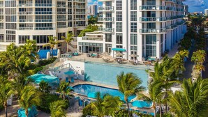 A modern hotel with a pool area, multiple balconies, and lush greenery.