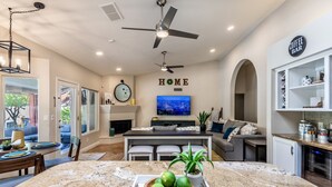 A modern kitchen with a granite countertop, a dining area with a table and chairs, a living room with a sofa and a TV, and a coffee bar area.