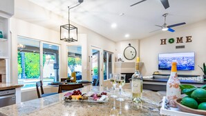 A modern kitchen with a marble countertop, a dining area, and a living room with a TV.