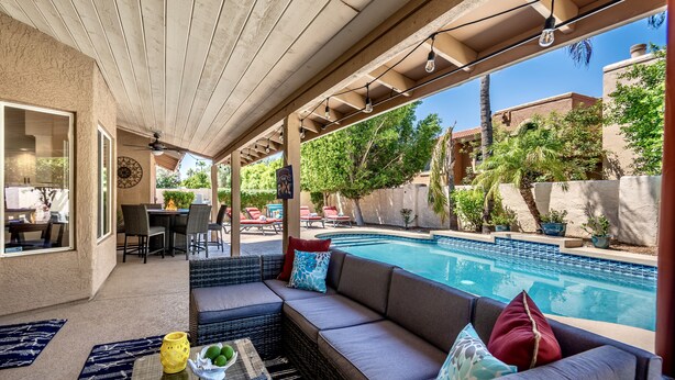 A covered patio area with a pool, outdoor furniture, and a view of the surrounding neighborhood.