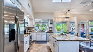 A modern kitchen with a stainless steel refrigerator, white cabinetry, and a large island with a marble countertop.