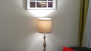 Una habitación con ventana que ofrece vistas de la ciudad, una lámpara de mesa, dos sillas con cojines rojos y una mesita auxiliar roja.