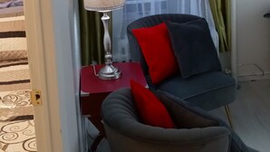 Una habitación con una silla, una mesa y una lámpara. Hay una ventana con cortinas.