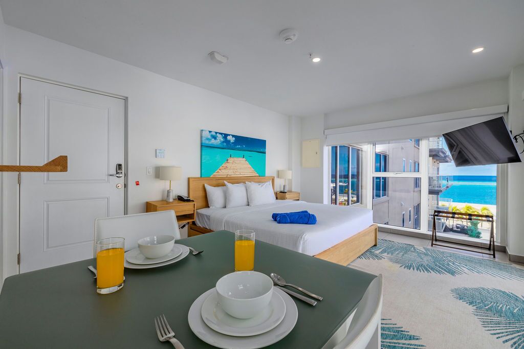 Ein Hotelzimmer mit Bett, einem Frühstückstisch, einem Fernseher und einem Balkon mit Meerblick.
