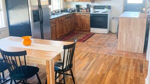 Una cocina con armarios de madera, un refrigerador de acero inoxidable, un lavamanos y una estufa. Hay una mesa de comedor con sillas y una alfombra.