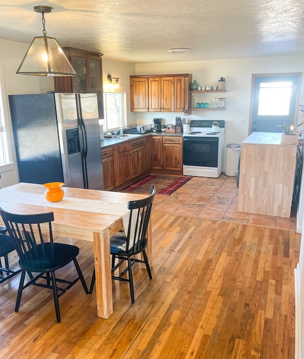 A kitchen with wooden cabinets, a stainless steel refrigerator, a sink, and a stove. There is a dining table with chairs and a rug.