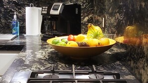 Une cuisine équipée d’une cuisinière à gaz, d’une machine à café et d’un saladier rempli de fruits posé sur le comptoir.