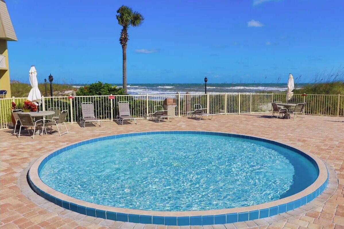 Une piscine avec vue sur l’océan, entourée d’une clôture et dotée d’un espace salon extérieur.