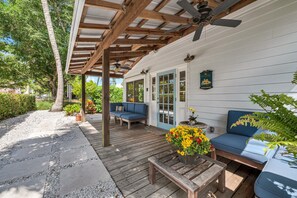 A covered patio with wooden flooring, two blue sofas, a wooden table, and a flower planter.