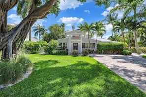 A two-story house with a well-maintained lawn, palm trees, and a clear blue sky.