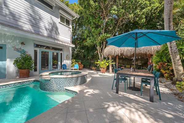 A swimming pool with a mosaic tile design, a thatched umbrella, and outdoor furniture.