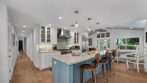Een ruime keuken met een groot eiland, witte kasten en een moderne kookplaat.