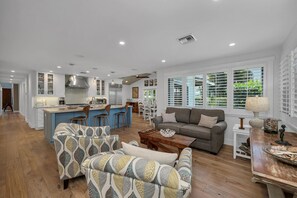 A spacious living area with a sofa set, a coffee table, and a dining area with a kitchen in the background.