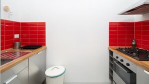 Pieni, käytännöllinen keittiö, jossa on punaiset laatat, kaasuliesi, pesuallas ja roskakori.