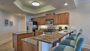 A modern kitchen with granite countertops, wooden cabinets, a built-in microwave, and a stainless steel refrigerator. - Dauphin Island Condo w/ Pool, Balcony & Ocean View (Dauphin Island)