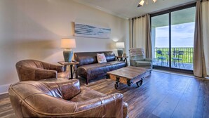 A spacious living room with a leather sofa, a coffee table, and a ceiling fan. - Dauphin Island Condo w/ Pool, Balcony & Ocean View (Dauphin Island)