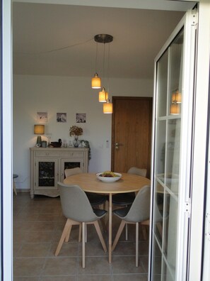 A dining area with a round table, four chairs, a bowl of fruit, a cabinet with a lamp, and a wooden door.