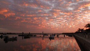 Un atardecer sobre un río tranquilo con barcos, un puente y un paseo marítimo.