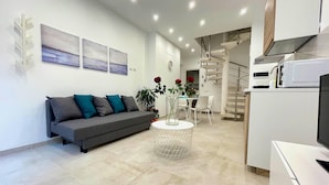 A modern living room with a grey sofa, a coffee table, and a dining area with a white table and chairs. - Appartamento Camera da Letto Vista Mare, 2 Bagni Parcheggio,spiaggia Solarium (Siracusa)