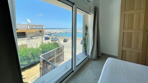 A room with a large window offering a view of a marina and boats, a wooden door, and a bed with a white cover. - Appartamento Camera da Letto Vista Mare, 2 Bagni Parcheggio,spiaggia Solarium (Siracusa)