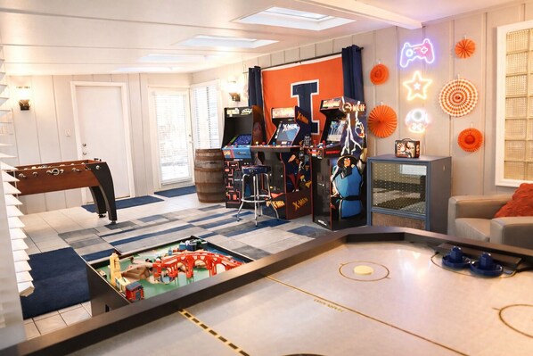 A room with a foosball table, arcade games, and a TV.
