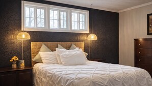 A bedroom with a large bed, two bedside lamps, a nightstand with a vase of flowers, and a dresser. - The Illini Game House (Champaign)