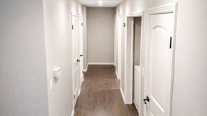 A hallway with white walls and wooden flooring, leading to multiple doors. - The Illini Game House (Champaign)