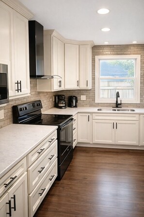 A kitchen with white cabinets, a black stove, a window, and a brick backsplash.