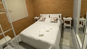 A neatly made bed with white linens and floral pillows, a whiteboard on the wall, and a small bedside table with a lamp. - Casa do Caminho (Praia da Vitoria)