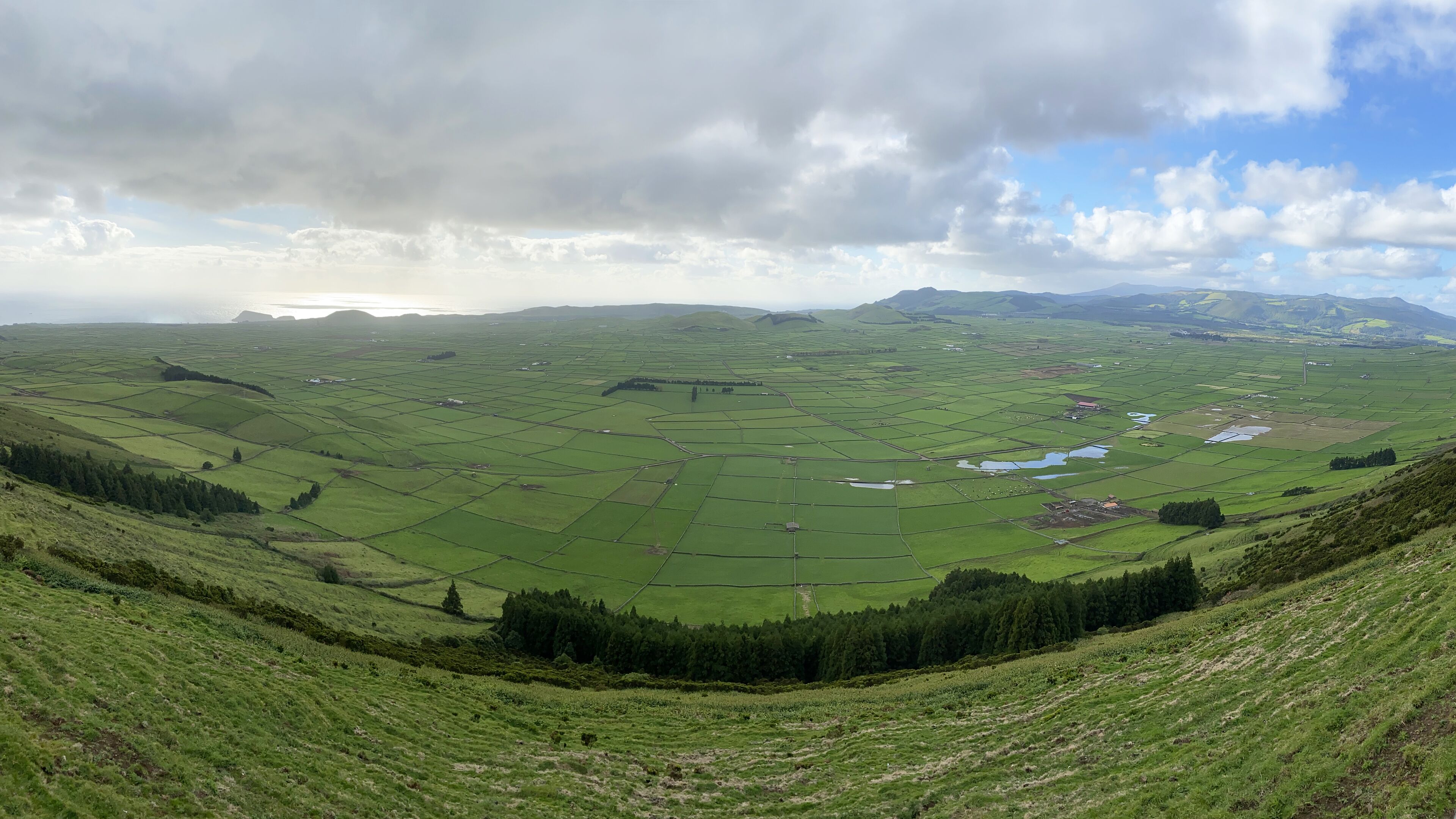 A panoramic view of a green valley with fields, a small body of water, and distant hills.