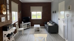 A living room with a TV, sofa, and a guitar on the wall. - Casa do Caminho (Praia da Vitoria)