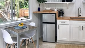 A modern kitchen with white cabinetry, a stainless steel refrigerator, a wooden countertop, and a window overlooking greenery. - Sun Filled, Tropical Bungalow (Haleiwa)