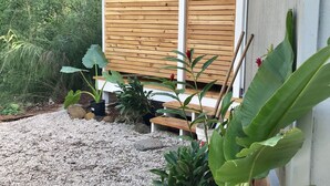 A covered outdoor area with a wooden fence, a gravel path, and various potted plants. - Sun Filled, Tropical Bungalow (Haleiwa)