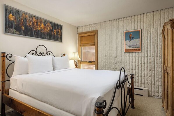 A neatly made bed with white linens in a room with a textured wallpaper, a framed picture on the wall, and a wooden headboard. - Vail 21 406 - 3 Bedroom Diamond (Vail)