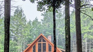 Une cabane en rondins dotée d’un balcon, entourée d’arbres.