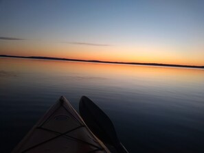 Kajakki tyynellä vedellä, taustalla auringonlasku.