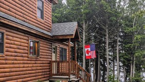 Une cabane en rondins avec un porche, un drapeau et une vue sur une forêt.