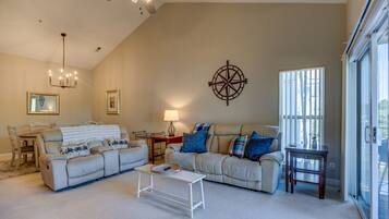 A living room with a sectional sofa, a coffee table, a lamp, a compass wall decoration, and a ceiling fan.