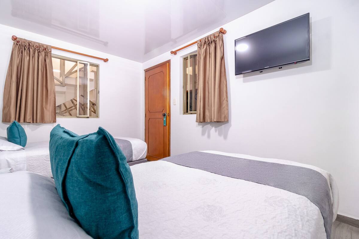 Una habitación de hotel con dos camas, un televisor montado en la pared y una ventana con cortinas.