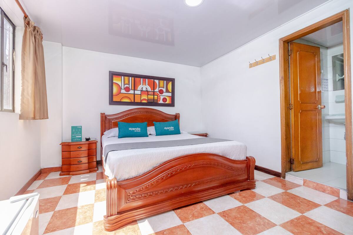 Un dormitorio con cama de madera, mesita de noche, cómoda y un cuadro en la pared.