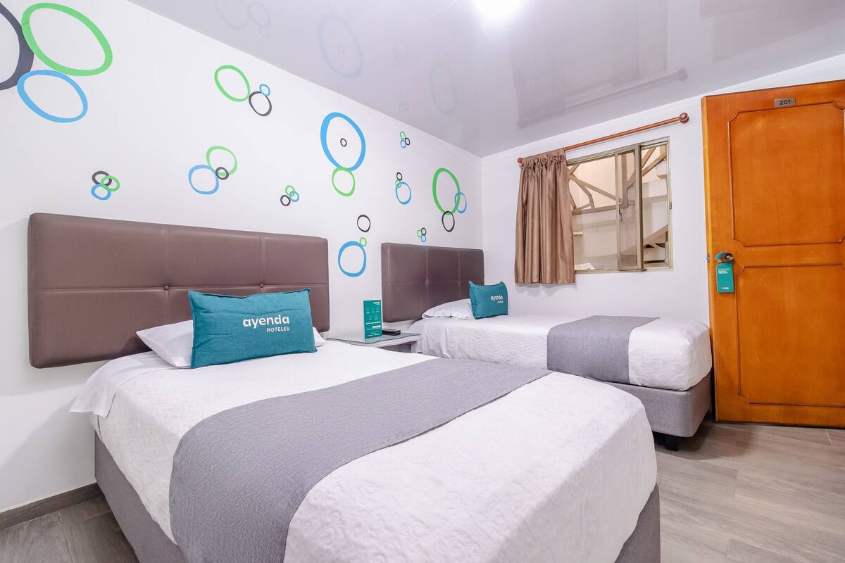 Habitación de hotel con dos camas, una puerta de madera y una ventana con cortinas.
