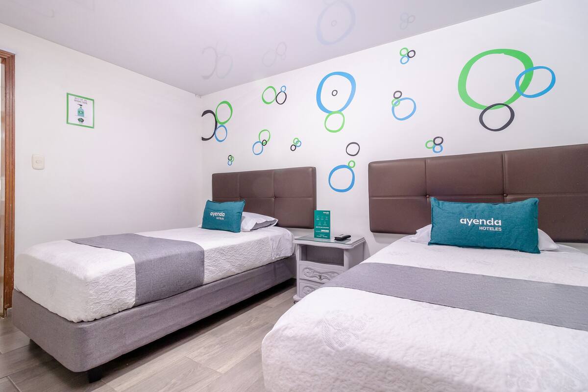Una habitación de hotel con dos camas, una mesita de noche y una pared con diseños circulares.