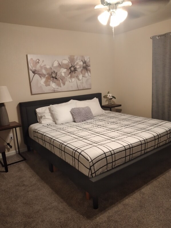 A bedroom with a bed, a nightstand, a lamp, a ceiling fan, and a floral painting on the wall. - Comfy Retreat  (Yuma)
